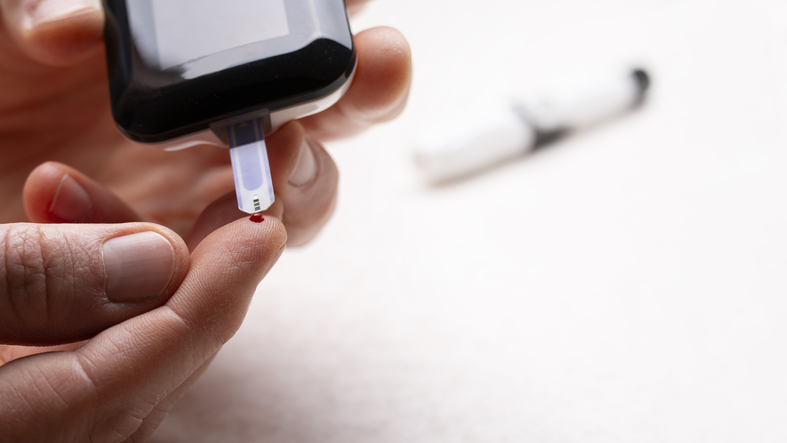 Pierced caucasian finger ready to measure glucose level by glucose meter closeup view. Diabetes awareness mockup with copy-space